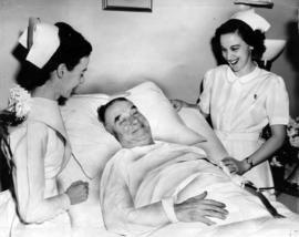 Gerald McGeer in hospital bed at St. Paul's, with two nurses at bedside