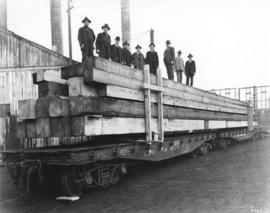 [Flatcar loaded with lumber, with nine men standing on top]