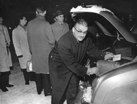 [A man puts Queen Elizabeth's luggage in the trunk of a car]