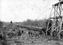 [Railway accident site, showing line of collapsed cars and workers clearing debris]