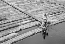 [A man fishing from a log boom]