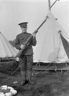 [Soldier with rifle in front of tent]