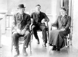 [Group portrait of 2 men and a woman seated on a porch]