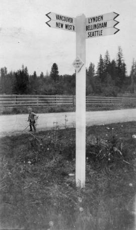 John Elkins standing on road nearby Vancouver Automobile directional signage