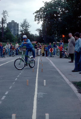 [Boy riding bicycle through obstacle course on running track]