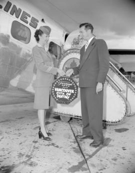 [Airline stewardess passing the "Vancouver, City of Destiny" film to a man at the airport]