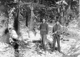 [Man and teenage boy posing with two deer strung from tree branch]