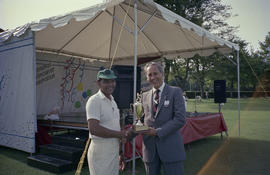 Two unidentified men with trophy in front of Centennial event tent