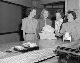 [Canadian Red Cross volunteer showing three women from the Junior League a bundle of linen or uni...