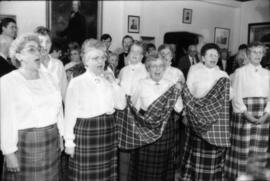 Group of women wearing tartan skirts singing and holding a piece of the Centennial tartan fabric