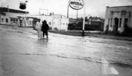 Two men standing in fIooded street in front of Imperial Dealer sign