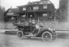 [Man and woman sitting in car in front of house]