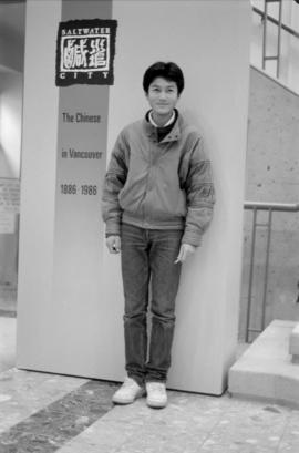 A colleague of Paul Yee's standing by a sign at the Saltwater City exhibit