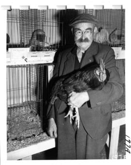 Man holding award-winning rooster in 1956 P.N.E. Poultry and Pet Stock competition