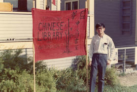 Young man standing with sign for the Strathcona Chinese Library and Information