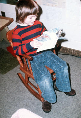 [Child in rocking chair reading a book]