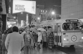 Christmas shoppers [group of people waiting in the rain to board the Victoria bus with people wal...