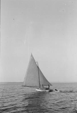 Three unidentified men in a sailboat pulling a row boat