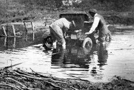 [Two men attaching a rope to William Gibson's car stuck in water]